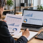 Une analyste examine un budget de projet CRM avec un ordinateur et une calculatrice.
