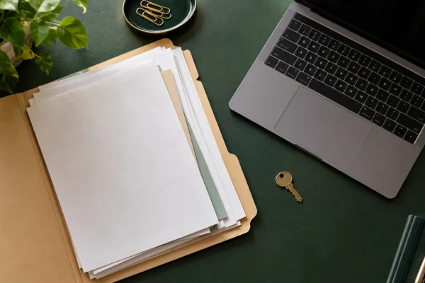 Dossier de documents près d’un ordinateur portable et d’une petite clé sur un bureau vert.